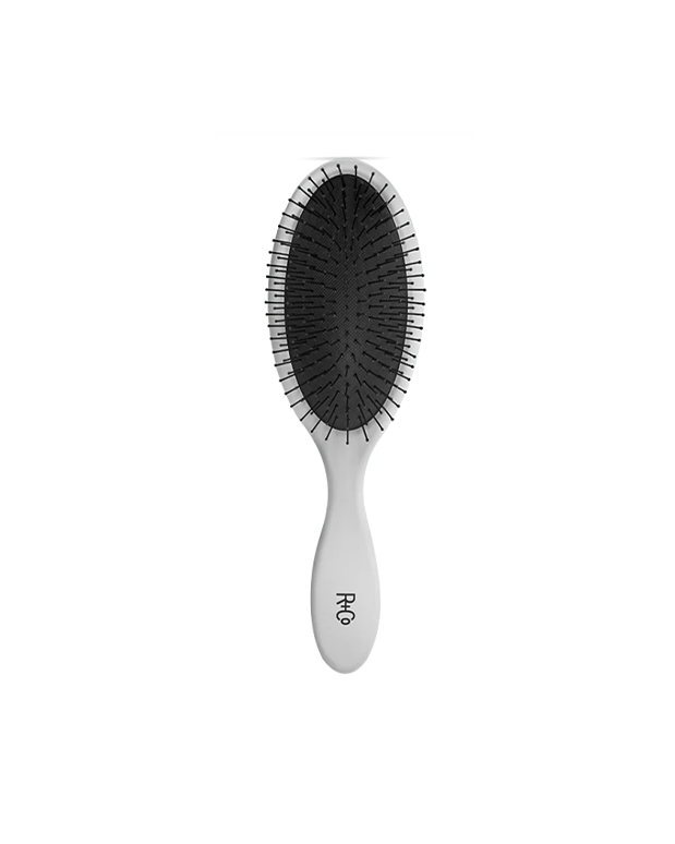 An ergonomic non-slip detangling hairbrush with a sleek grey handle and black bristles, featuring the R+CO logo.
